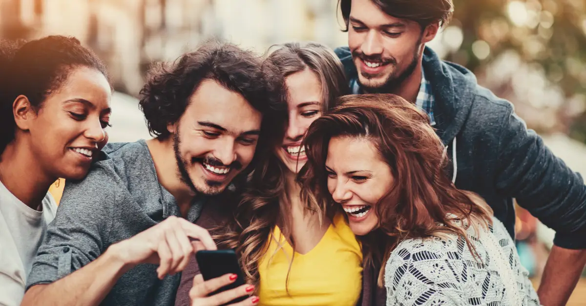 A group of people laughing while looking together at a phone.
